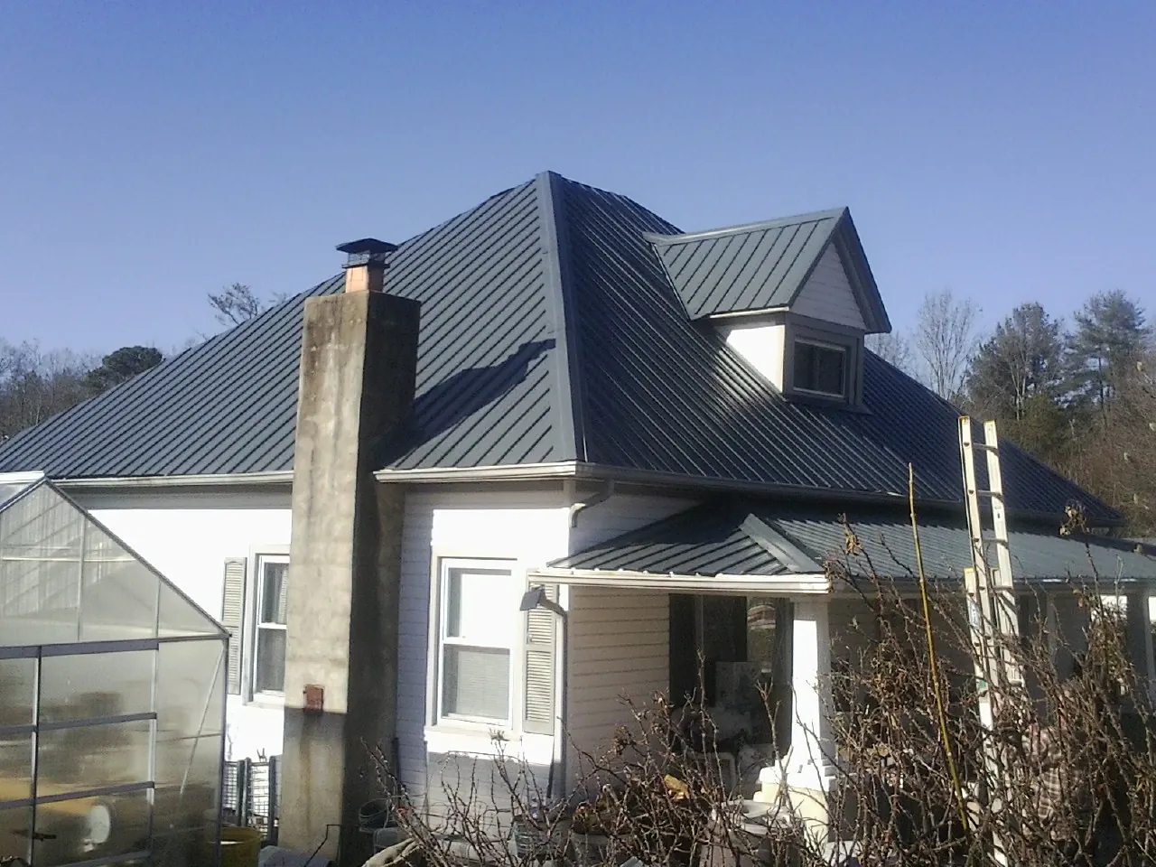 Dark blue standing seam metal roof on a white farmhouse with dormer — Slate & Tile Roof Repair by Roofing Brothers in West Hempstead