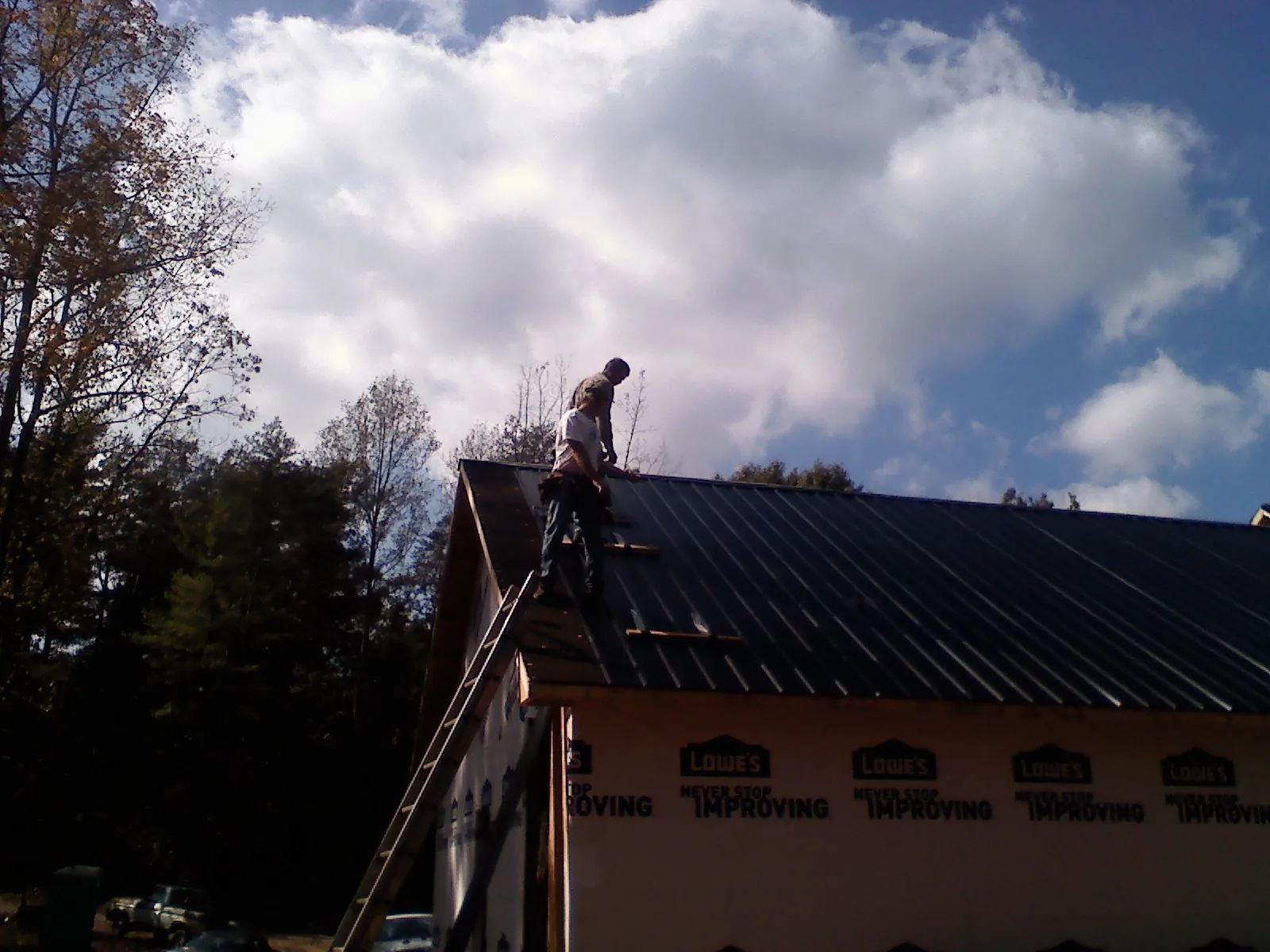 Roofer fastening dark metal panels high against a cloudy sky, from a Roof Inspection job in West Hempstead