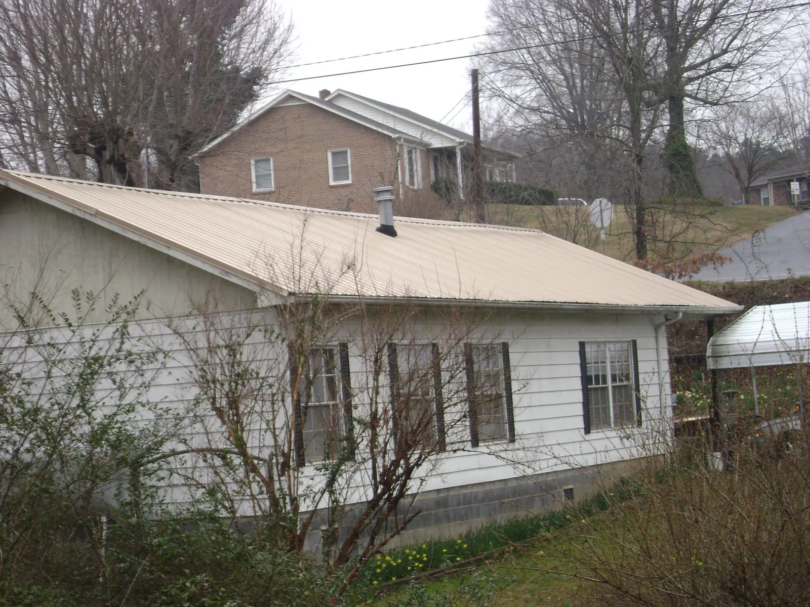 Tan metal roof on a white sided house set into a hillside — Commercial Roofing by Roofing Brothers in West Hempstead